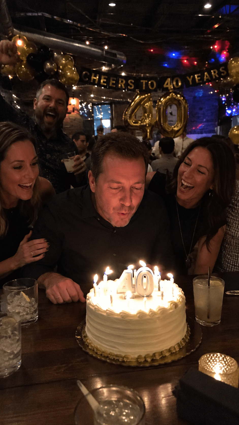 Friends celebrating a fortieth birthday around a candlelit cake